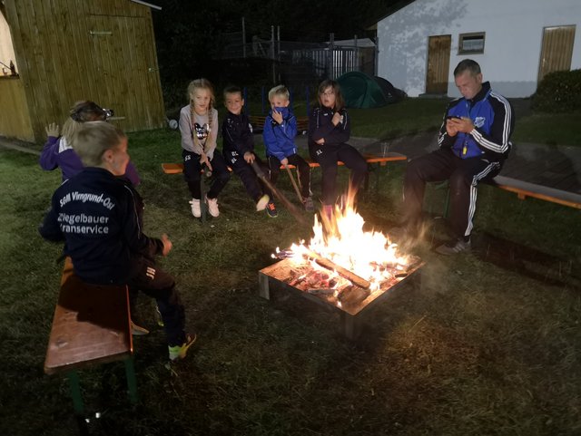 Kinder sitzen um ein Feuer und grillen